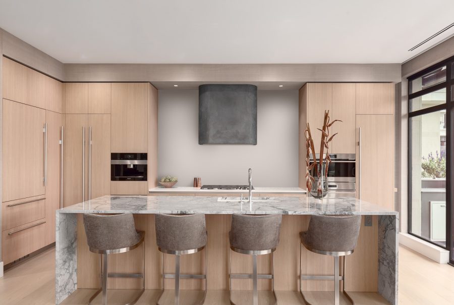 Penthouse kitchen with waterfall marble island, natural wood cabinetry, and custom concrete hood fan