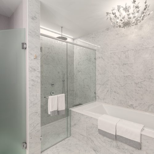Luxury penthouse bathroom with marble walls and floors, freestanding bathtub, frameless glass shower, and floral light fixture