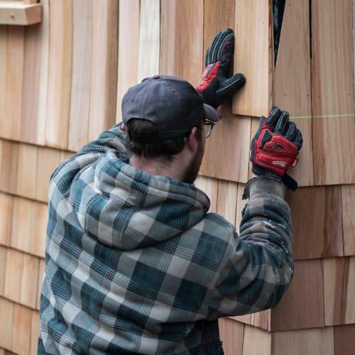 Construction worker installing cedar shingles with laser level on exterior wall