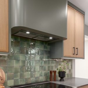 Modern kitchen renovation with stainless steel range, green tile backsplash, and custom wood cabinetry.